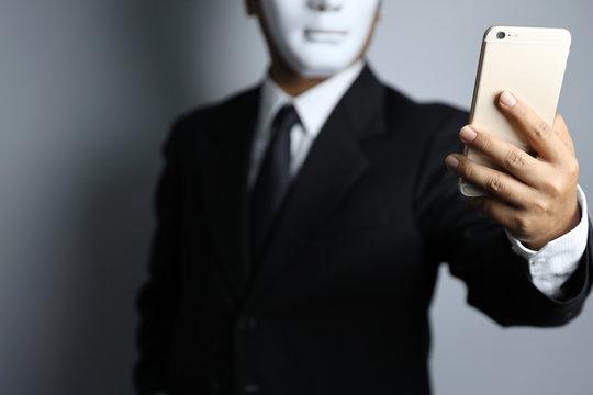 Employee Or Businessman Wearing Black Suit And Mask With Cell Phone Hacking And Stealing Big Data