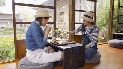 two happy girls tourists doing chado tea ceremony sitting indoor japanese style wooden house by spring peaceful green garden outdoor. young women travelers pour tea into bowl sitting on floor relax.