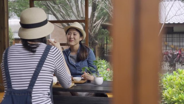 two happy asian women friends eating desserts together indoor wood house by japanese style spring teien garden. young girls toursit talking drinking tea doing chado ceremony chatting laughing relax