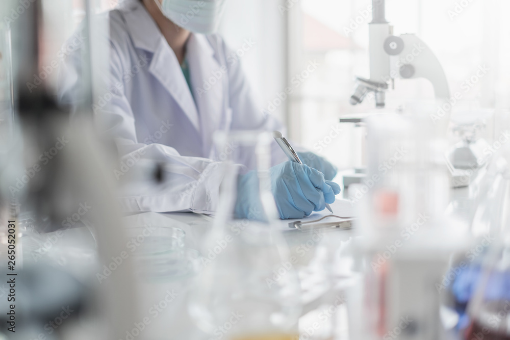 Wall mural a scientist hands writing on a clipboard in laboratory with test tube microscope and solutions.