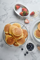 A stack of pancake with blueberries, strawberries, orange on white marble table. Breakfast menu, top view