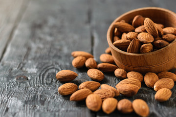 Almonds spill out of a wooden bowl on a black wooden table.