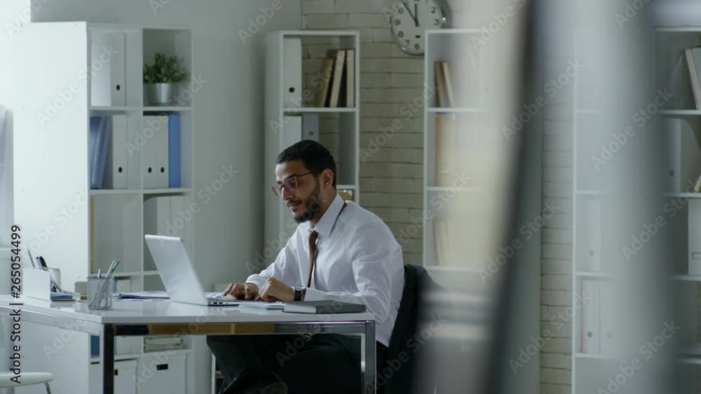 Poster tracking shot of professional middle eastern businessman in eyeglasses using laptop computer while w
