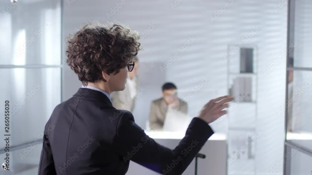 Poster businesswoman with short curly hair tapping on invisible multi-touch interface on glass wall in offi