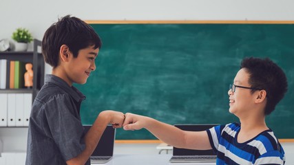 Asian happy school boy with friend celebrating with a fist bump on black board background with smiling face.Creative education of kid student concept.