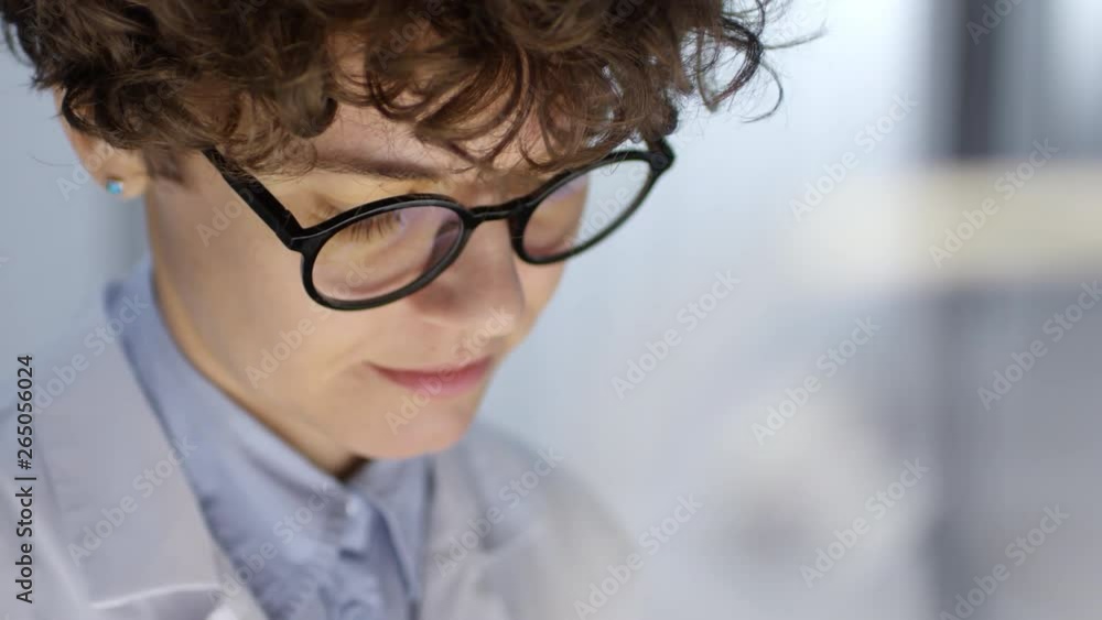 Poster close up shot of female scientist in lab coat and glasses watching something on transparent monitor 