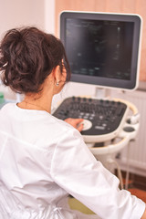 Mature doctor doing ultrasound diagnostics of patient. Doctor wearing in white unifrom looking at screen