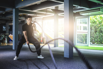 Asia man exercising with battle ropes at gym..