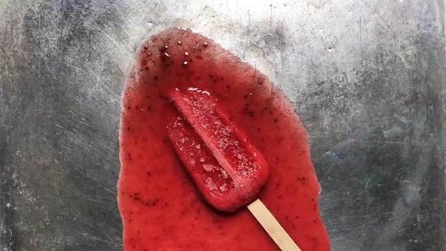 Melting red strawberry Popcicle icecicle sorbet ice cream bar on stainless steel background - Melting ice cream footage 