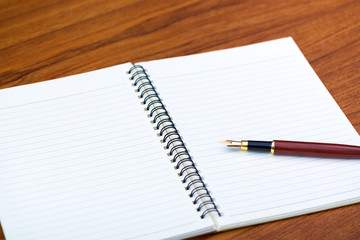Fountain pen or ink pen with notebook paper on wooden working table with copy space, office desk concept.