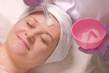 Obraz na płótnie Canvas Relaxed woman with eyes closed on a cosmetological procedure. Applying a transparent nutritional gel on the face of a smiling middle-aged woman. Anti-aging skin treatment, health and beauty.