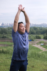 Korean man stretches against the background of the city. Healthy lifestyle. Adult man  practicing yoga in nature.