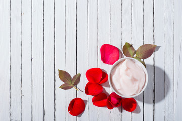 moisturizer and rose petals with shade on white wood