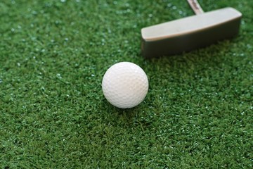Golf ball and putter on green lawn background