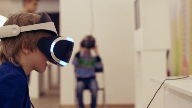 Children in an interactive VR helmet play video game. Boy in VR glasses of virtual reality playing game. 