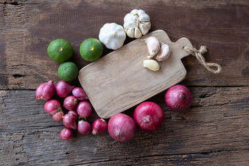 Top view of herbal vegetable ingredients, garlic, red onion, lime, lime leaf and chopping board on old wooden table, cooking preparation concept
