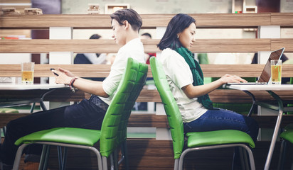 Asian teenagers schoolchildren boy and girl sit in a cafe at different tables and look at social...
