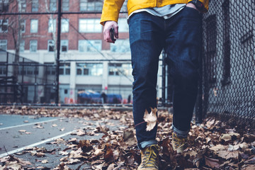 Close-up of man's legs wearing jeans and yellow raincoat walking among fallen leaves