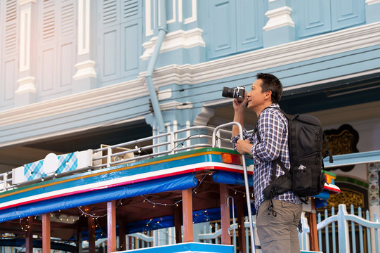 Tourist on local bus in phuket old town. Asian man  with backpack holding a vintage camera hanging on the back of pho thong local bus on debuk road with sino portuguese architecture building .