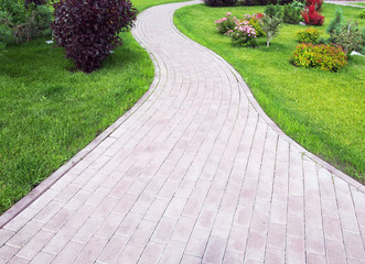Curved footpath paved with bricks running ahead along a green grassy lawn. Landscaping design