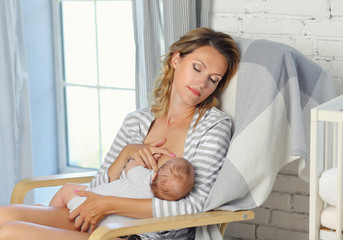 A young mother breast-feeds a newborn sitting in a chair in striped clothes.
