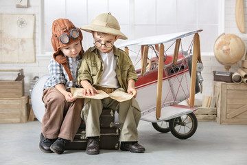 Little boys in the form of a pilot and a tourist play near the toy-plane in the room