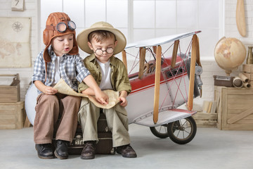 Little boys in the form of a pilot and a tourist play near the toy-plane in the room