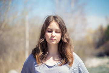Fototapeta premium Young girl with positive emotions. Relaxed, pleased with a smile on her face. Spring natural background, forest and river.