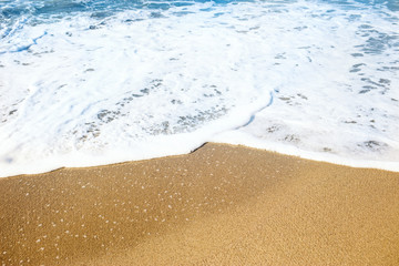Sandy beach and soft blue ocean wave with white foam.