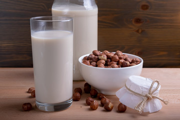 Glass of Hazelnut milk and bottle and organic hazelnuts on wooden background, Alternative Milk. Nuts milk