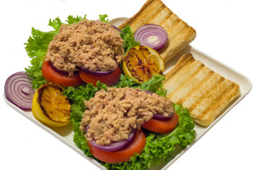 Tuna sandwiches and vegetables on a white square plate. Isolated on white background.