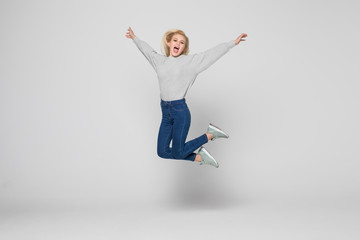 Full length portrait of a cheerful young woman jumping and celebrating over gray background