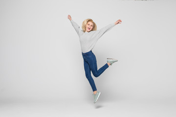 Fototapeta premium happiness, freedom, movement and people concept. Smiling young woman jumping in air isolated on gray background