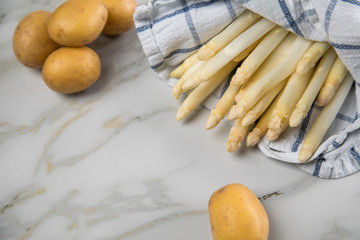 Roher, weißer Spargel in Tuch und Kartoffeln auf Marmor Hintergrund