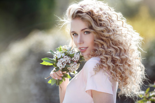 Beautiful young model spring girl in flowers with hairstyle in summer blossom park. Woman in a blooming garden. Fashion.Portrait of a beautiful woman with curly hair outdoors in a spring park