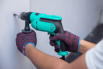 Handyman with drill on white wall close up