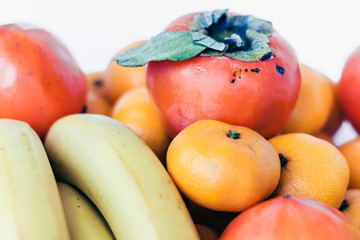 A selection of arranged different fresh fruits of bananas, mandarins, persimmons and lemons on white background close up.
