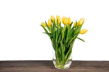 Fresh bouquet of yellow tulips in vase on a wooden table against white background.