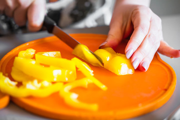 Frau in der küche schneidet gelbe Paprika für salat 