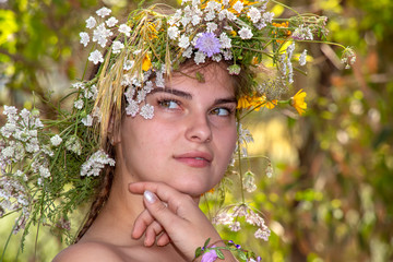 Portrait of a young woman in a wreath of flowers closeup with a dreamy expression on her face