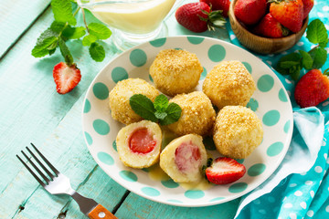 Cottage cheese dumplings with fresh strawberry, served with sour-honey sauce, delicious summer dessert on the kitchen wooden table. Copy space.
