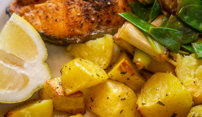 Close-up of salmon cutlet with potatoes on spring onions and sugar snap peas