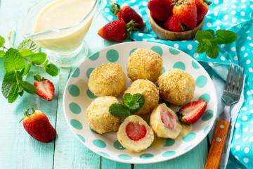 Cottage cheese dumplings with fresh strawberry, served with sour-honey sauce, delicious summer dessert on the kitchen wooden table.