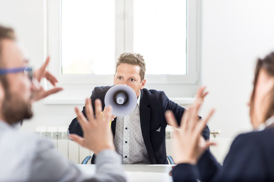 Young boss shouting at employees through megaphone in conference room.
