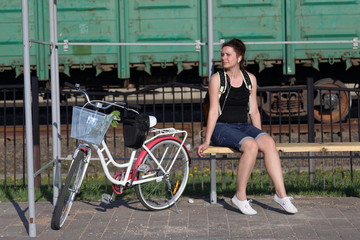 Fototapeta na wymiar A girl sits on a bench and listens to music. Nearby is her bike.