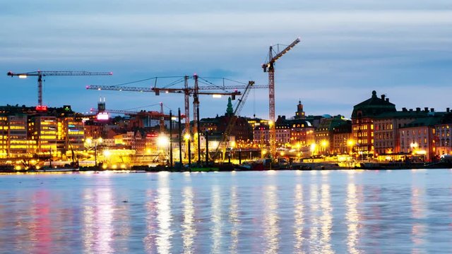 Stockholm, Sweden. Time-lapse of Gamla Stan with construction cranes during the sunset. View of boats and cloudy sky in the evening and night, zoom in