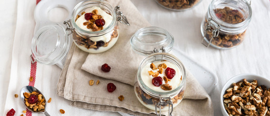 Obraz na płótnie Canvas Crunchy honey granola in jars with flax seeds, cranberries, coconut, yogurt and cherry. Healthy, vegeterian fiber food. Breakfast time. Dieting concept for banner. Copy space