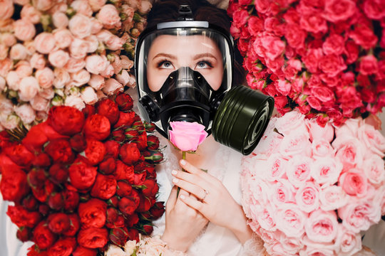 Young Woman Is Smelling Flowers In A Gas Mask. Allergy And AsthmaTreatment Concept.