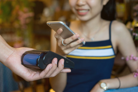 close up business owner man hand using payment machine for receiving money form woman customer's smartphone  in the cafe , contactless payment concept
