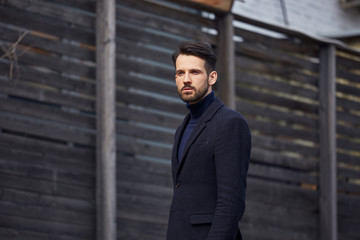 Fashion beard style business handsome male model posing in style clothing blue jacket and trousers on street wooden wall outdoors background. Closeup